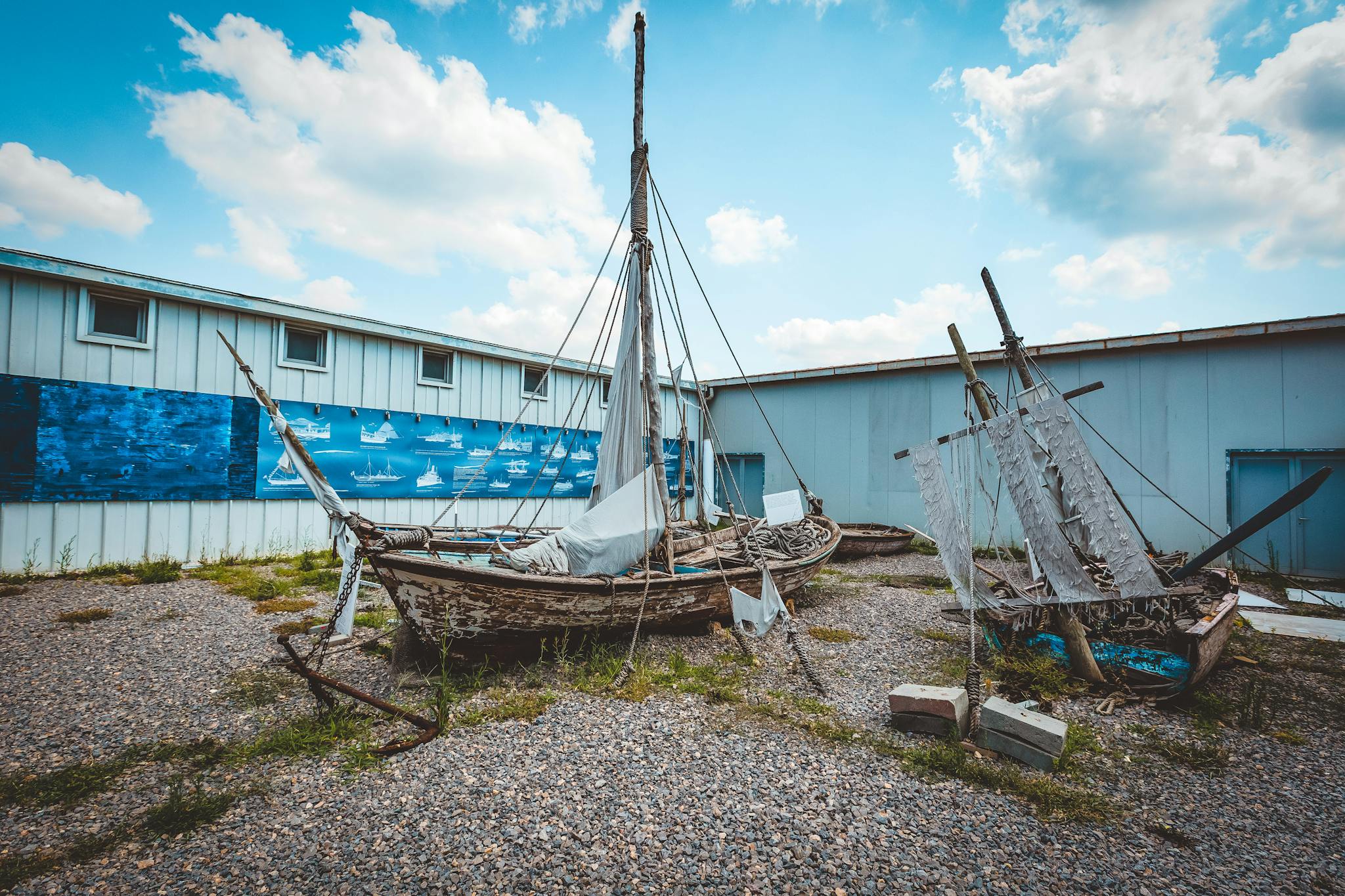 Old wooden sailboats in an outdoor yard against a blue sky, showcasing maritime history.